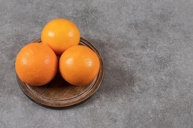Закройте вверх по фото спелых апельсинов на деревянной доске над серым столом.