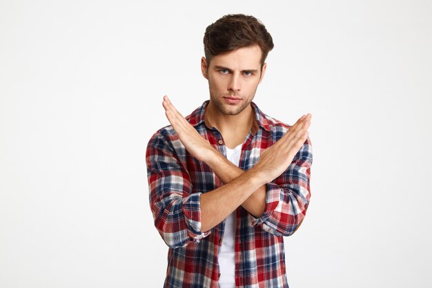 Close-up photo of serious handsome young man showing stop gesture with crossed hands