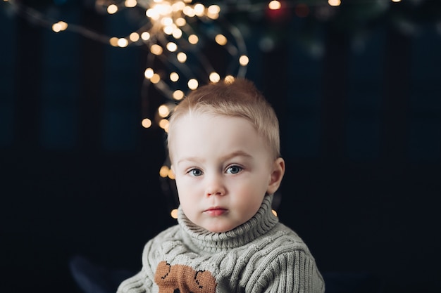 Close-up photo of a serious little kid with Christmas lights in background