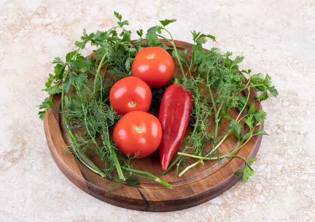 Close up photo of tomatoes and pepper with greens on wooden board.
