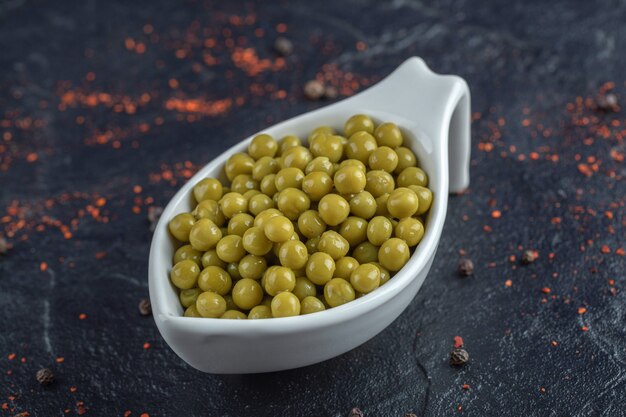 Close up photo of white bowl full with green peas.