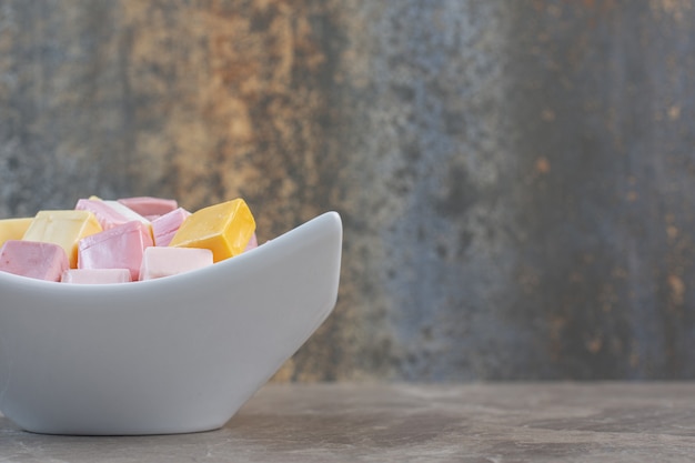 Free photo close up photo of white ceramic bowl full with colorful cubic candies. pink, white and yellow candies.