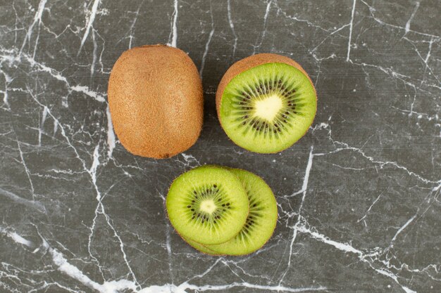 Close up photo of whole and sliced kiwi on black.