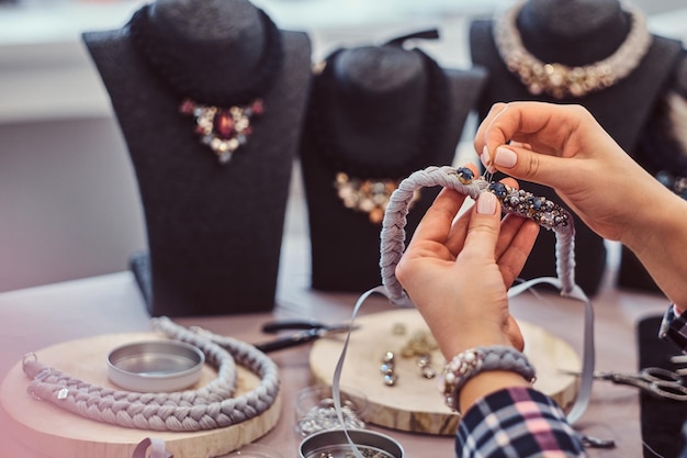 Крупный план женских рук, которые делают ожерелья ручной работы, работая с иглами и нитками в ювелирной мастерской.