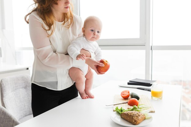 부엌에서 요리하는 동안 귀여운 아기를 안고 서 있는 여성의 사진을 클로즈업