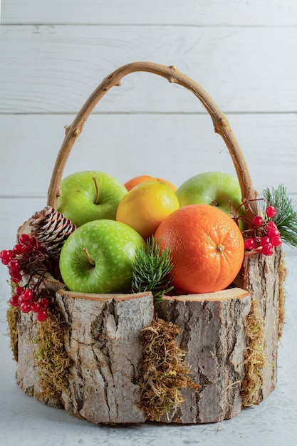 Close up photo of wooden basket full with different fruits on grey surface. 