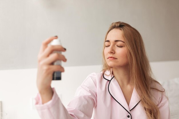 Close up photo of young lady sitting on bed and holding spray in hand at home