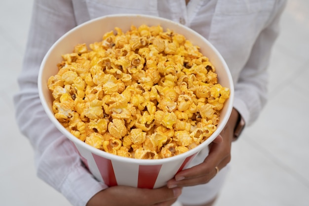 Close-up photo of a young sweet girl, who is holding a tube of popcorn in her hands.