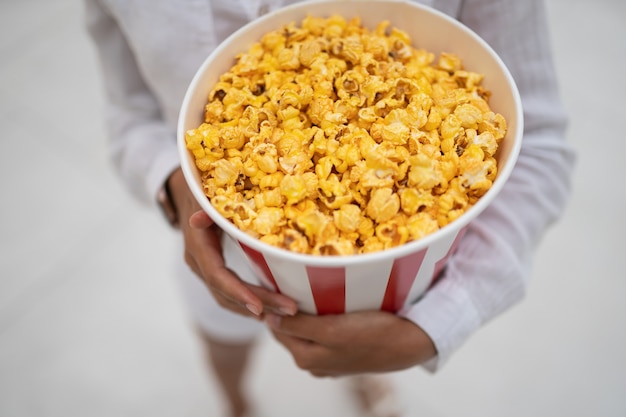 Close-up photo of a young sweet girl, who is holding a tube of popcorn in her hands.