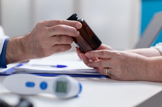 Close up of physician giving bottle of pills to old patient at annual checkup visit. Hands of doctor holding jar with prescription medicine and treatment to help cure illness. Medical remedy