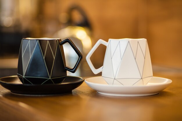 Крупный план черной керамической чашки на черной тарелке и белой керамической чашки на белой тарелке находится на коричневом столе