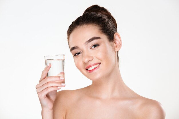 Close up picture of glad gorgeous woman being half-naked drinking minaral water from transparent glass with smile