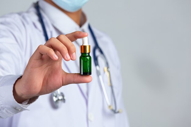 Close up picture of medical doctor holding a bottle of cannabis oil on white wall.