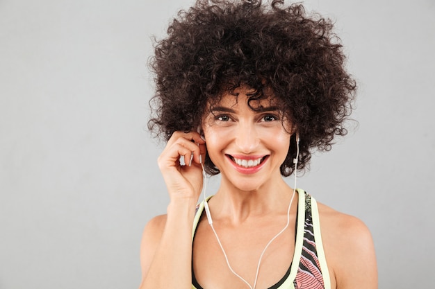 Закройте изображение улыбающегося кудрявой фитнес женщина прослушивания музыки