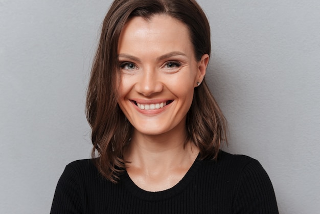 Close up picture of smiling woman in black dress looking at the camera on gray