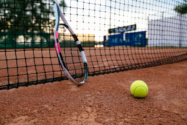 Крупным планом изображение теннисной ракетки и мяч на глиняном дворе. Просмотр через сеть.