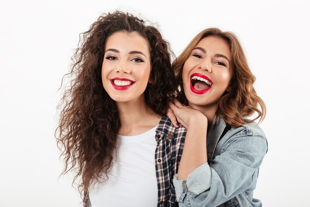 Close up picture of two cheerful girls posing together  over white wall