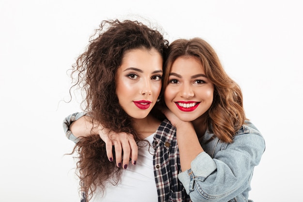 Close up picture of two smiling girls posing together  over white wall