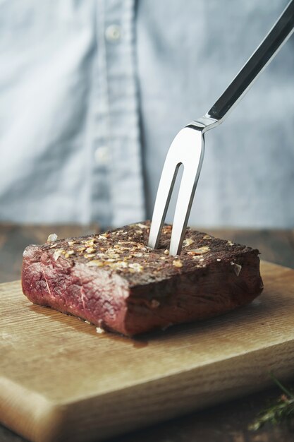 Закройте кусок жареного мяса на деревянной доске со стальной большой вилкой в нем
