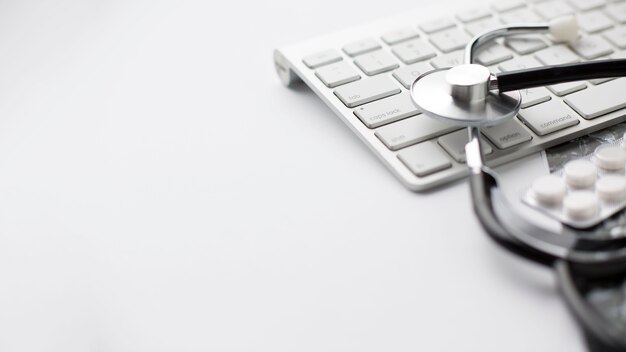 Close-up of pill's blister pack and stethoscope on keyboard over white surface