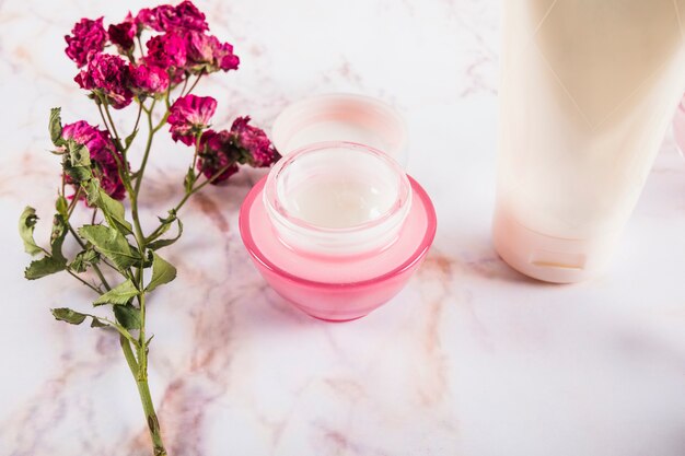 Close-up of pink flowers near skin care creams on marble