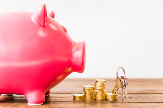 Close-up of pink piggybank near stacked coins and key