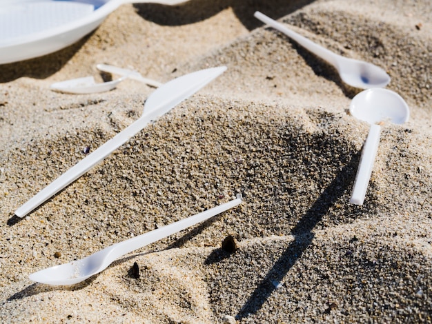 Крупный план пластиковых столовых приборов на песке на пляже
