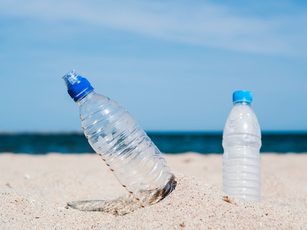 プラスチック製の水のボトルのクローズアップはビーチで砂で立ち往生