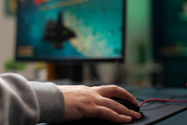 비디오 게임을 하기 위해 책상에 마우스 패드가 있는 마우스를 들고 있는 플레이어를 닫습니다. 컴퓨터에서 게임 장비를 사용하고 온라인 게임을 하는 남자. 게임을 즐기는 가제트에 있는 플레이어의 손