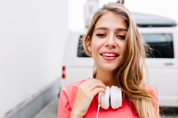 Close-up portrait of adorable blonde girl walking on the street in big white earphones
