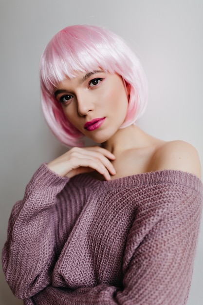 Close-up portrait of adorable caucasian female model wears elegant colorful peruke. Stunning lady with light-pink hair dreamy posing on light wall.