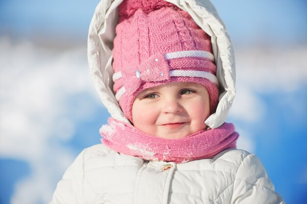 Close up portrait of adorable female child in warm winter clothing poses against snow