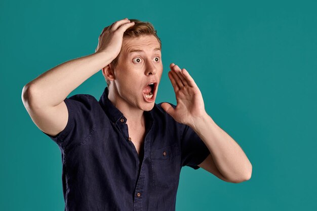 Close-up portrait of an adult good-looking ginger fellow in a stylish navy t-shirt looking shocked while posing on blue studio background. Human facial expressions. Sincere emotions concept. Copy spac