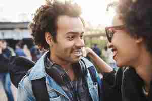 Free photo close-up portrait of african-american couple in trendy clothes and afro haircuts, hugging while smiling and looking at each other, standing in park. couple in love spending weekends outdoors.