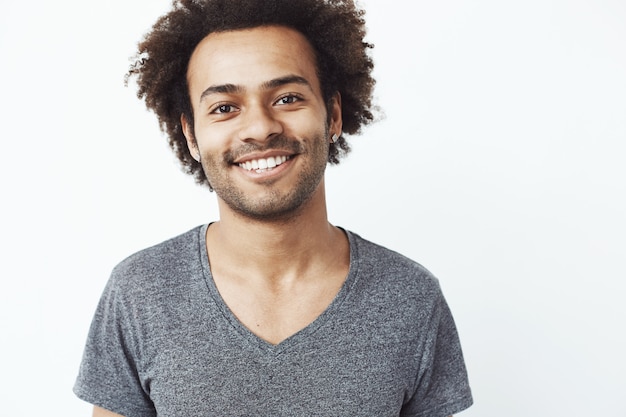 Primo piano ritratto di ragazzo africano sorridente, uno studente fiducioso nella sua carriera futura, o un sogno cacciatore di teste in piedi sul muro bianco.