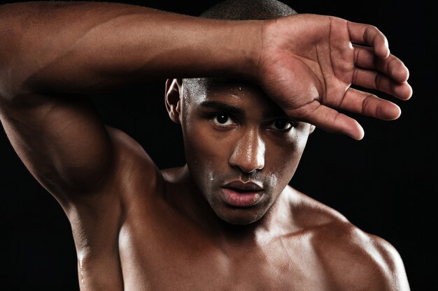 Close-up portrait of afro american sports man, resting after workout, wipes sweat from his forehead