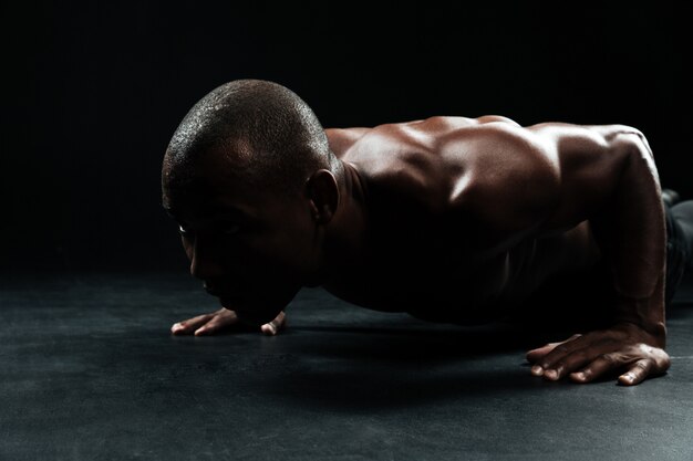 床に腕立て伏せ運動をしている美しい筋肉の体で、アフロアメリカンスポーツ男のクローズアップの肖像画