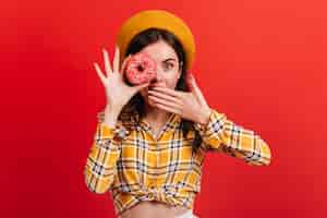 Free photo close-up portrait of amazed green-eyed girl holding tasty donut. lady in beret and shirt covers her mouth.