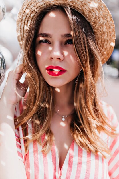 Close-up portrait of amazing european woman with cute hairstyle posing with interested face expression. Adorable caucasian girl in straw hat looking away.
