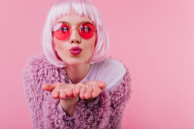 Foto gratuita ritratto del primo piano di incredibile modello femminile in parrucca rosa che invia un bacio d'aria. ragazza di buon umore in occhiali da sole e peruke