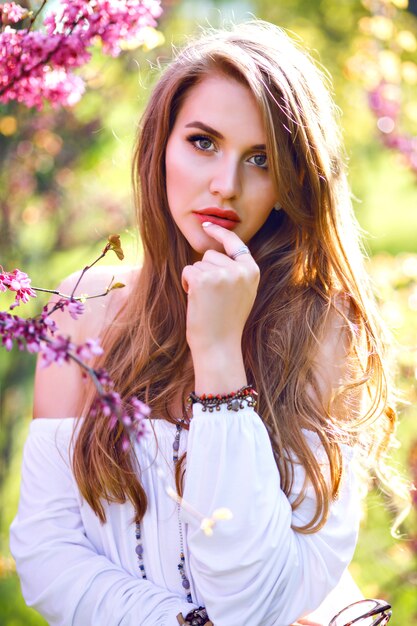 Close up portrait of amazing magazine tender woman with natural long hairs and perfect skin posing at blooming garden, spring time.