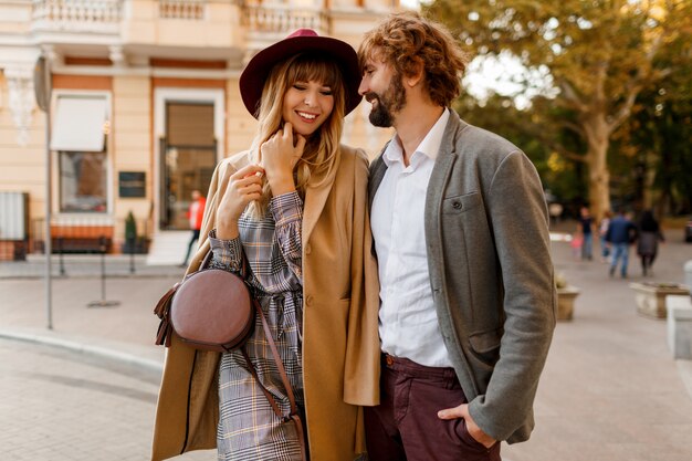 Close up portrait of amazing stylish couple in love spending romantic holidays in European city. Pretty blond woman in hat and casual dress smiling and looking on her handsome man with beard.
