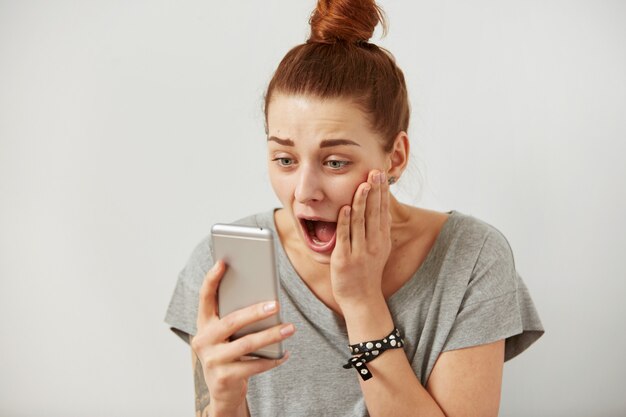 Close up portrait anxious or shocked young freelancer woman looking at phone seeing bad news