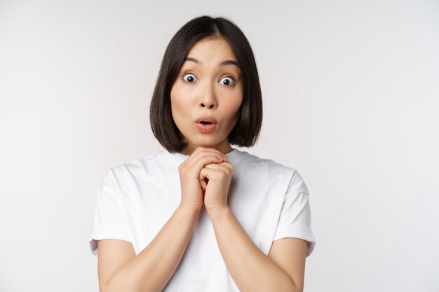 Close up portrait of asian brunette woman looking amazed say wow watching smth impressive standing over white background