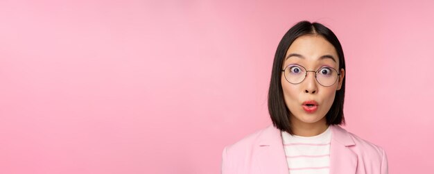 Close up portrait of asian businesswoman in glasses looking surprised at camera amazed reaction stan