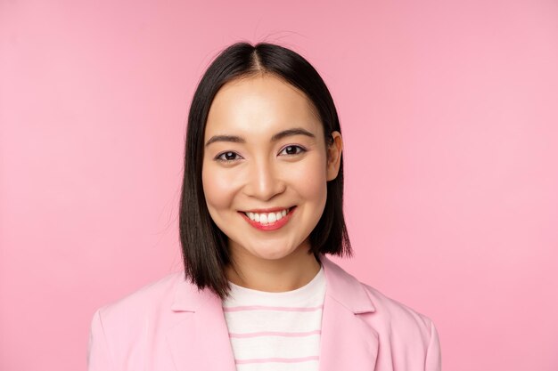 Close up portrait of asian corporate woman looking professional smiling at camera wearing suit standing over pink background Copy space