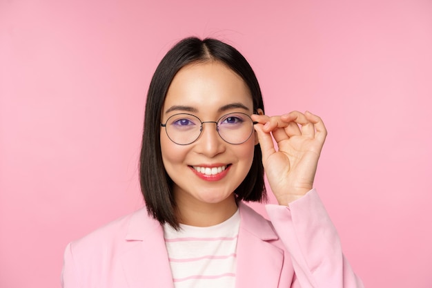 Close up portrait of asian corporate woman professional businesswoman in glasses smiling and looking confident at camera pink background