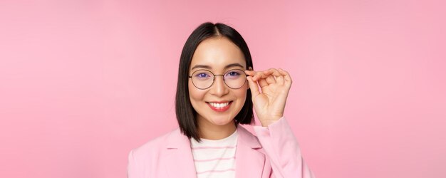 Close up portrait of asian corporate woman professional businesswoman in glasses smiling and looking confident at camera pink background