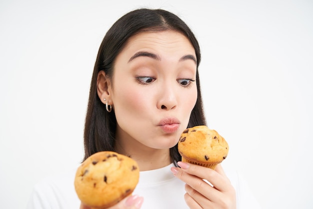 アジアの女の子が白い背景で隔離の幸せそうな顔でカップケーキを食べるの肖像画を間近します。