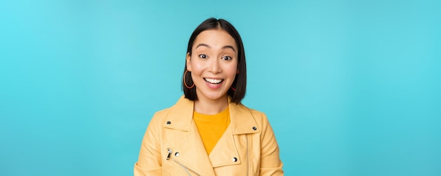 Close up portrait of asian girl looks surprised at amazed wow face expression stands over blue background